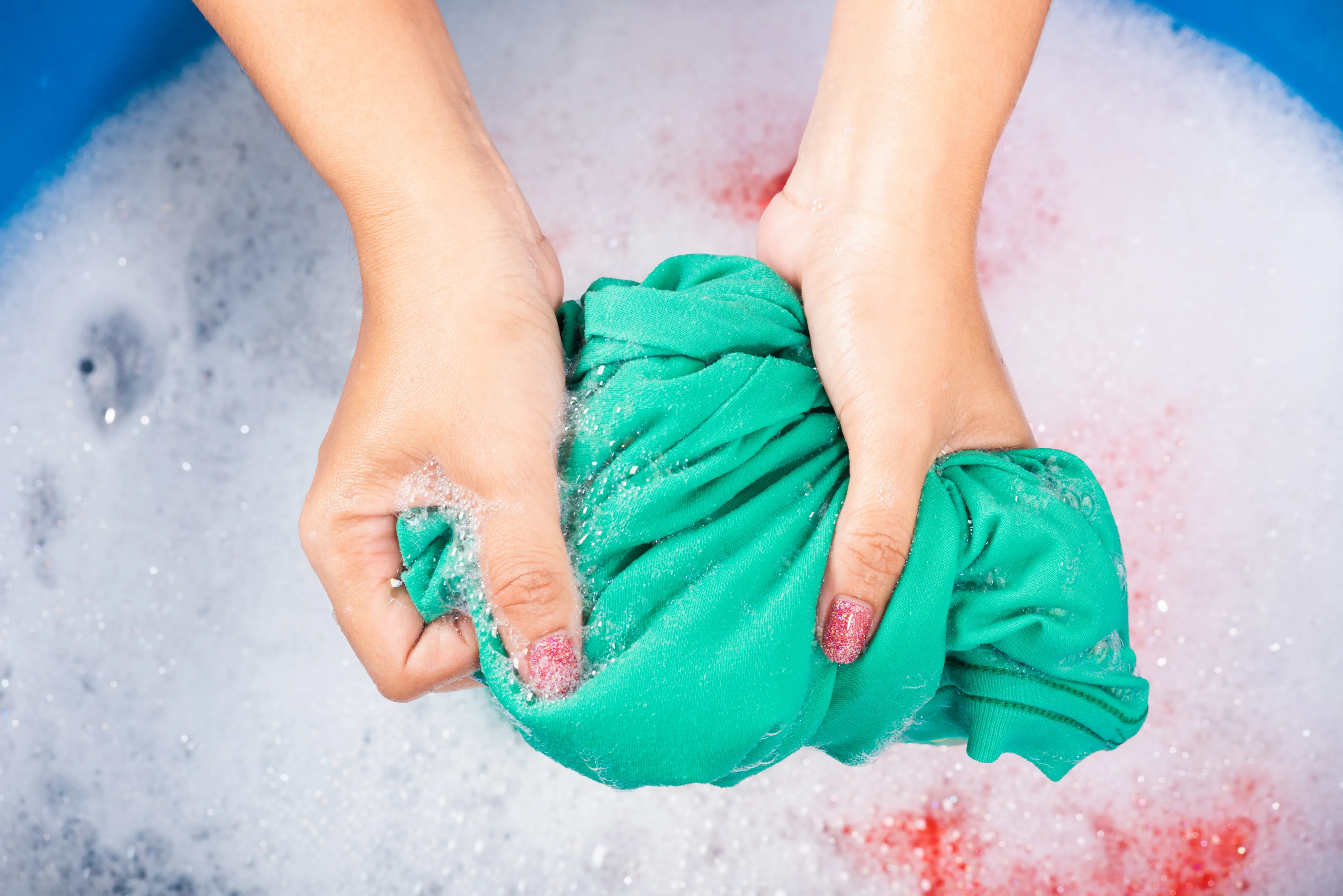 Mãos segurando uma peça de roupa verde na água