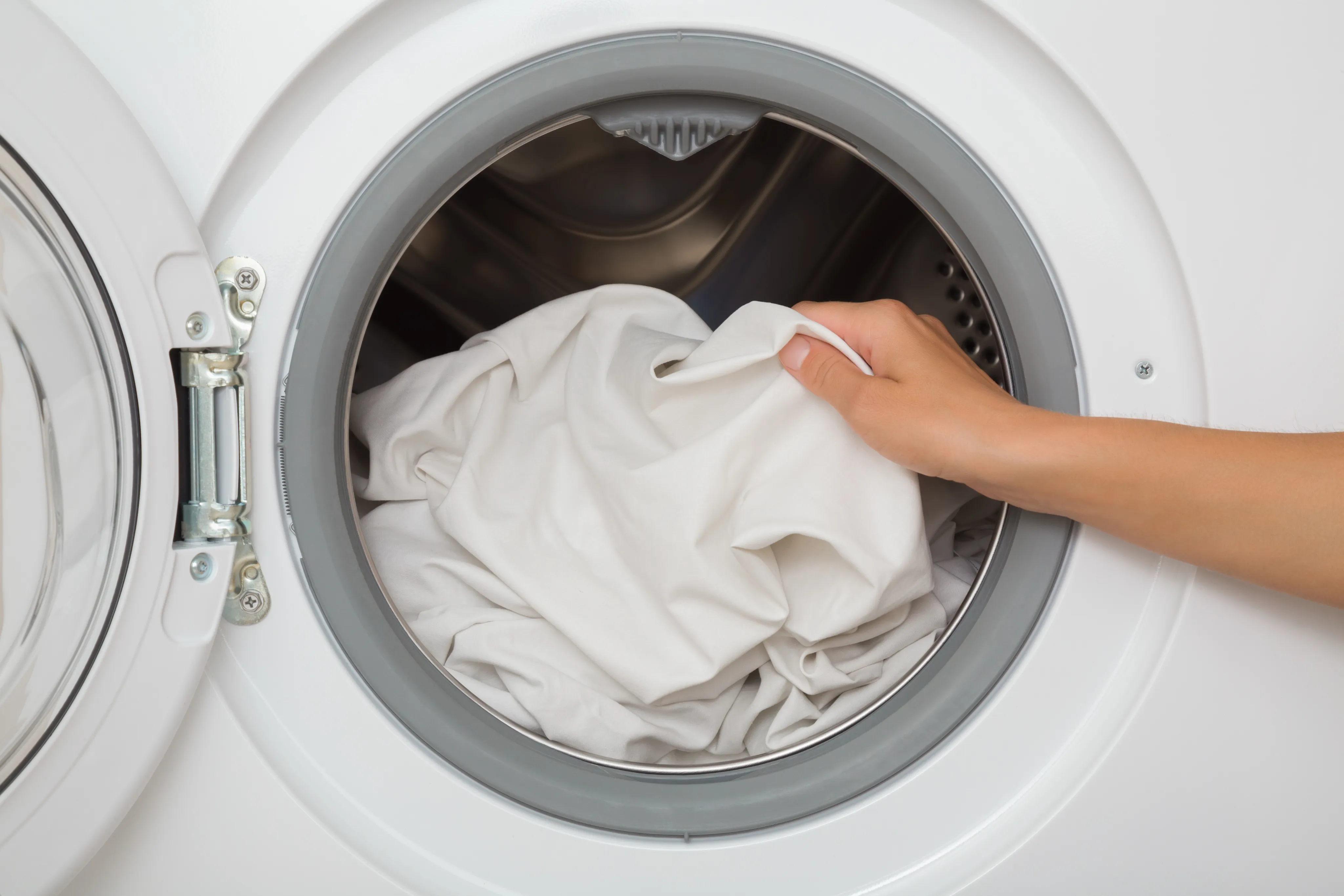 Mão colocando roupa branca na máquina de lavar